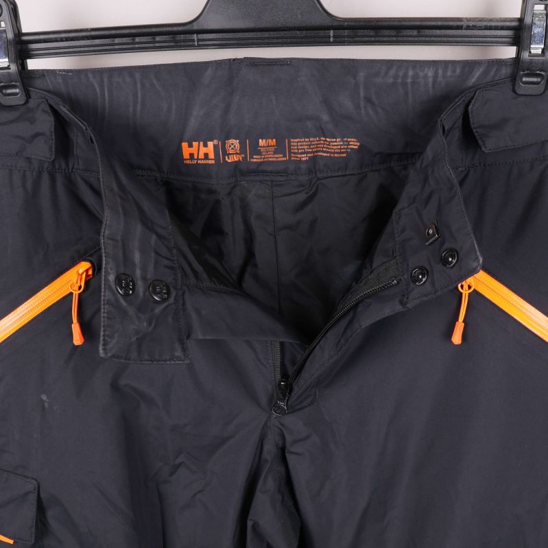 Närbild på midja och dragkedjor i orange på svarta byxor