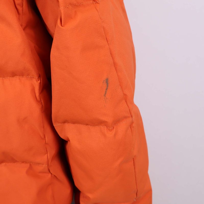 Närbild på mörk smutsfläck på orange jackas vänstra ärm