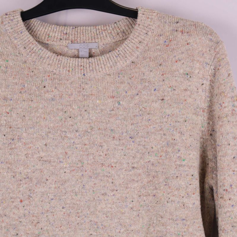 Närbild på halsringning och axel på beige melerad tröja