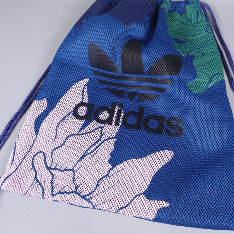 Närbild på blå adidaspåse med svart logga och blommigt mönster