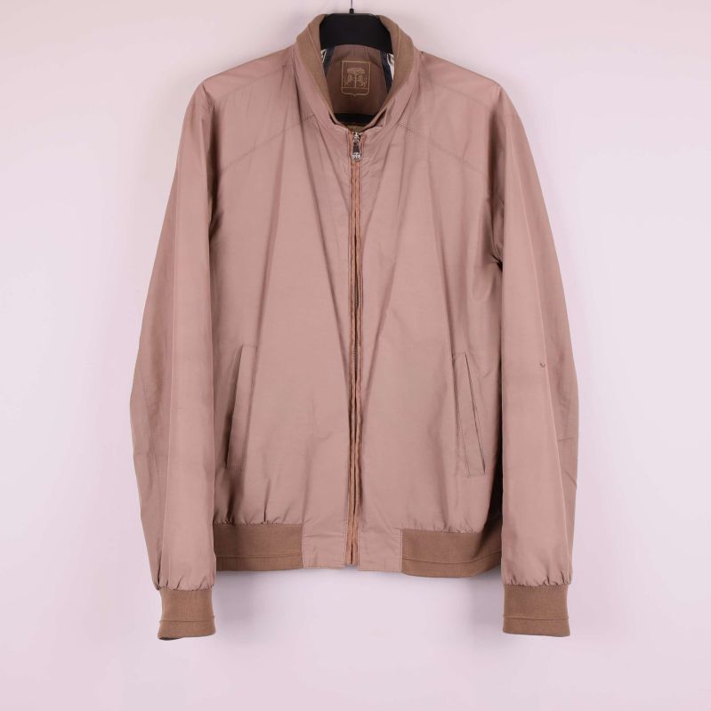 Beige bomberjacka hänger på galge mot ljus bakgrund