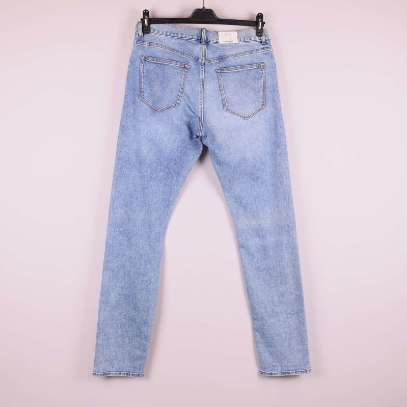 Jeans i ljus denim upphängda på galge, helbild bakifrån