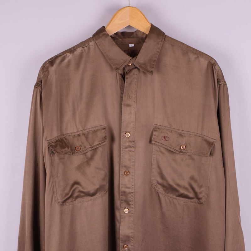 Närbild på övre delen av brun silkesskjorta med fickor och knappar