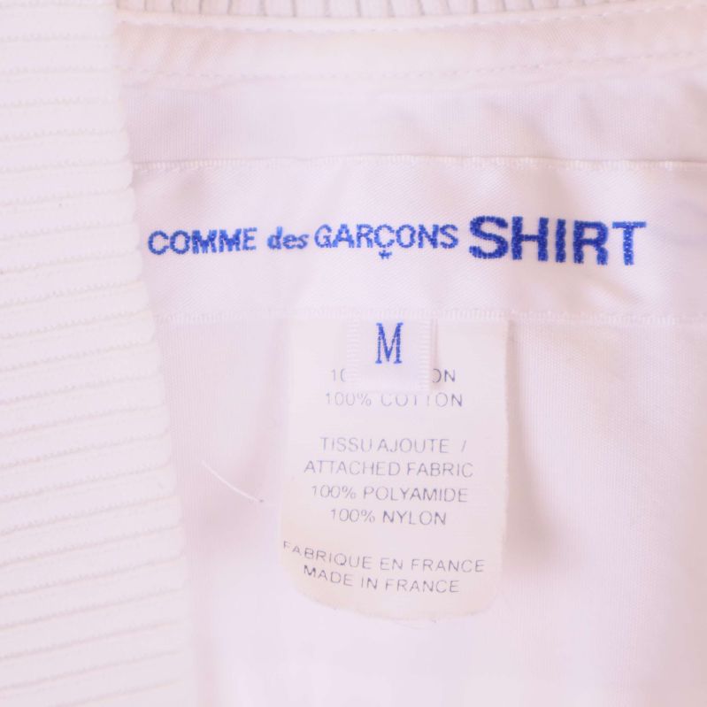 Närbild på märkesetikett med Comme des Garçons Shirt och storlek M