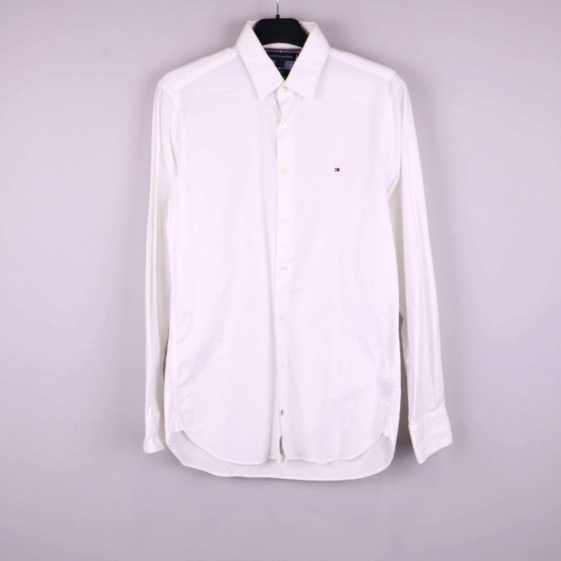 Vit långärmad skjorta på galge mot ljus bakgrund