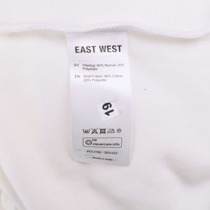 Materiallapp med EastWest-text, visar 80% bomull och 20% polyester