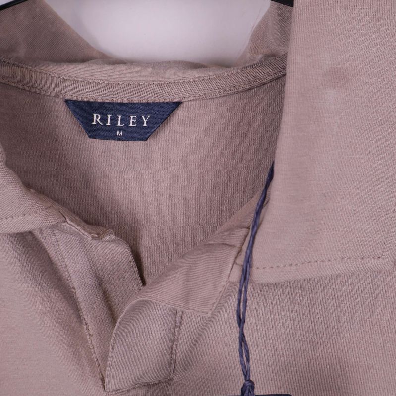Närbild på Riley-logga och krage på beige pikétröja