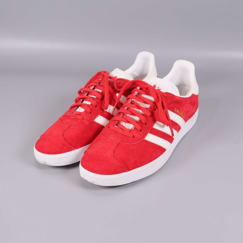 Röda sneakers med vita ränder och sula, sedd framifrån