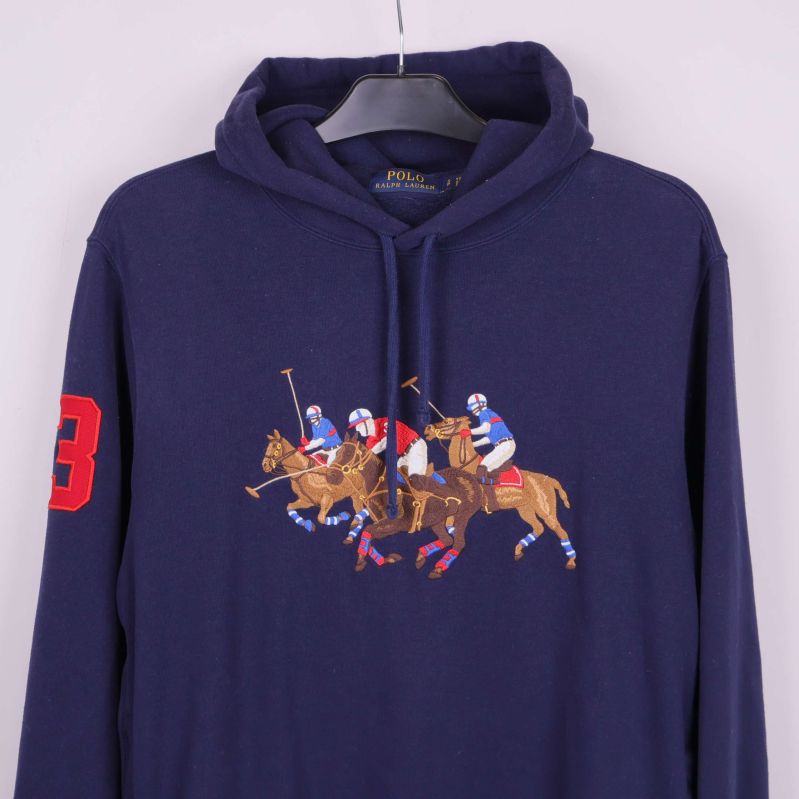 Närbild på broderat polospelmotiv och röd siffra på ärmen