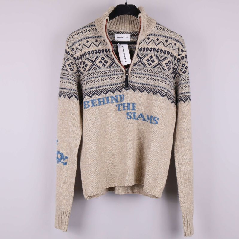 Framsidan av beige stickad tröja med blå mönster och text