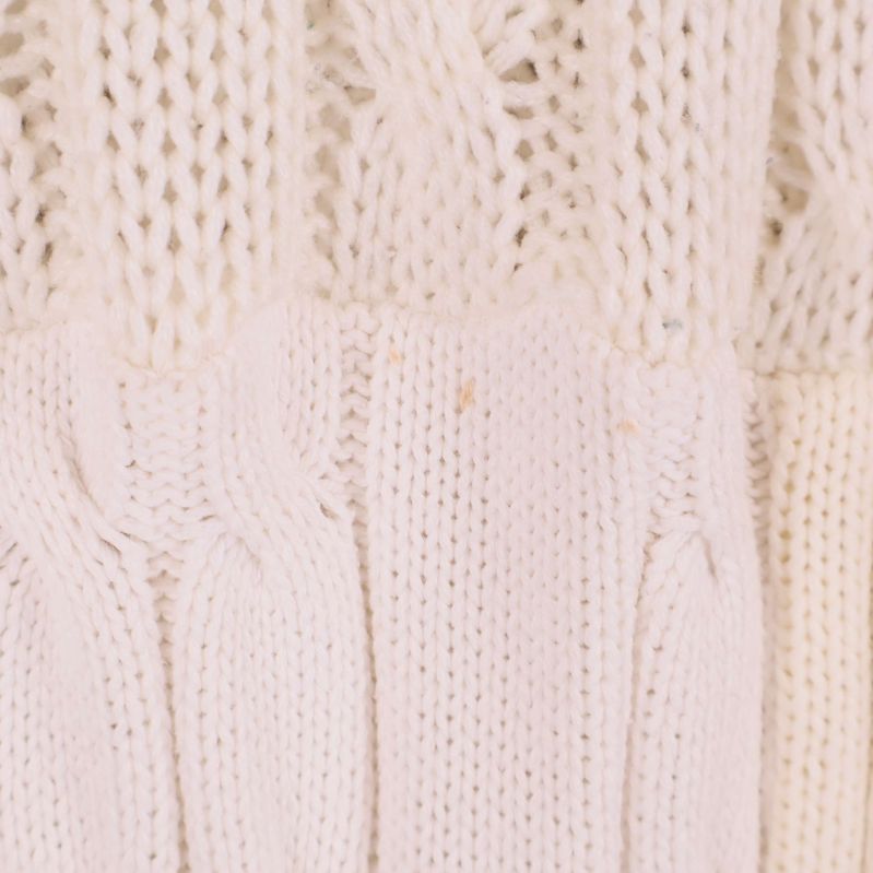 Närbild på gräddvit stickning med små fläckar på tröjklänning