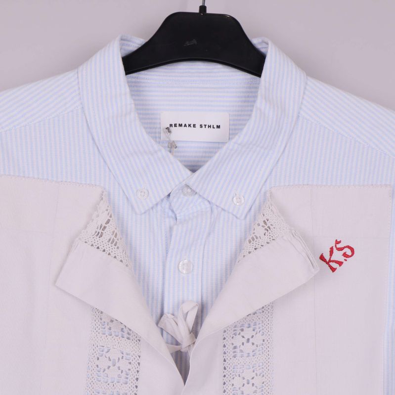 Närbild på krage och spetsdetaljer med broderat monogram