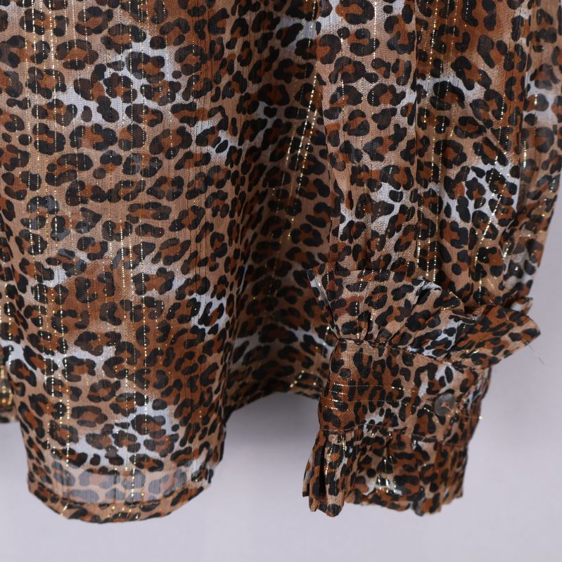 Närbild av leopardmönster och gulddetaljer på blus