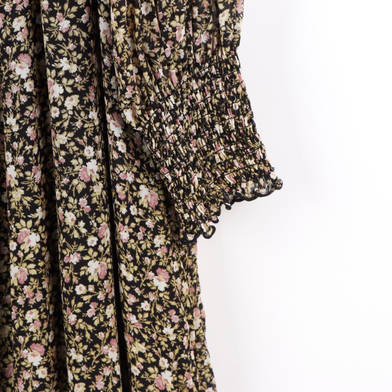 Detaljbild av blommigt mönster och smockärm på klänningen