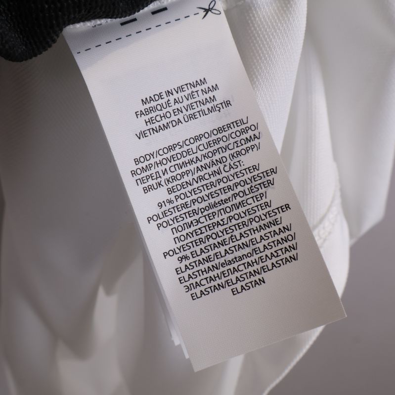 Materialetikett på vit pikétröja visar polyester och elastan