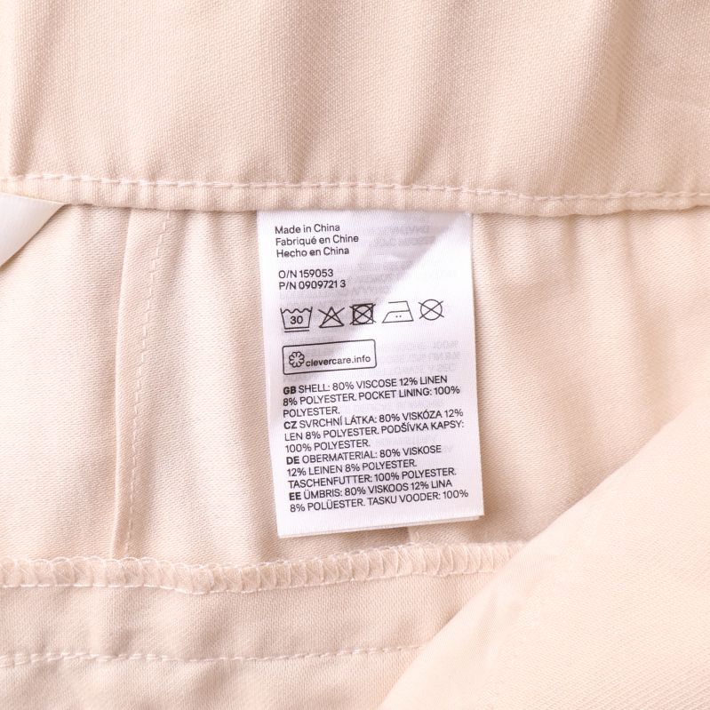 Två etiketter med materialinformation i beige byxor