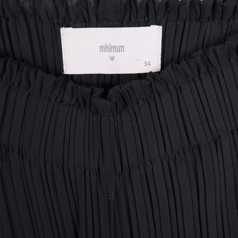 Närbild på midjelinning och etikett på plisserade byxor