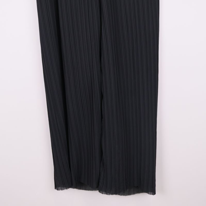 Närbild på ben och fåll av svarta plisserade byxor