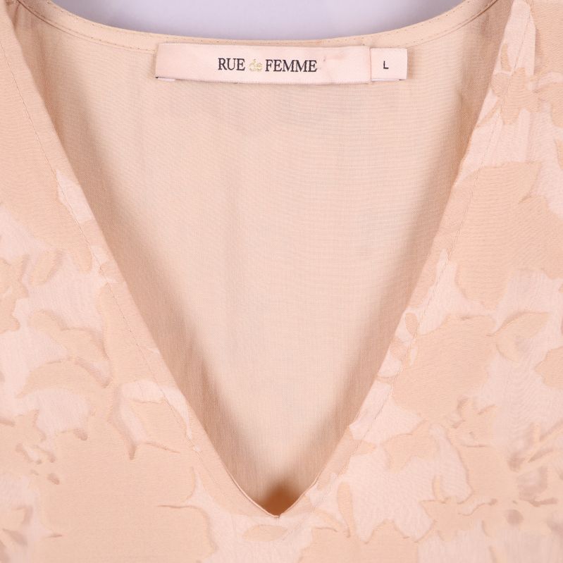 Närbild på v-ringning och varumärkestag i beige blommig klänning