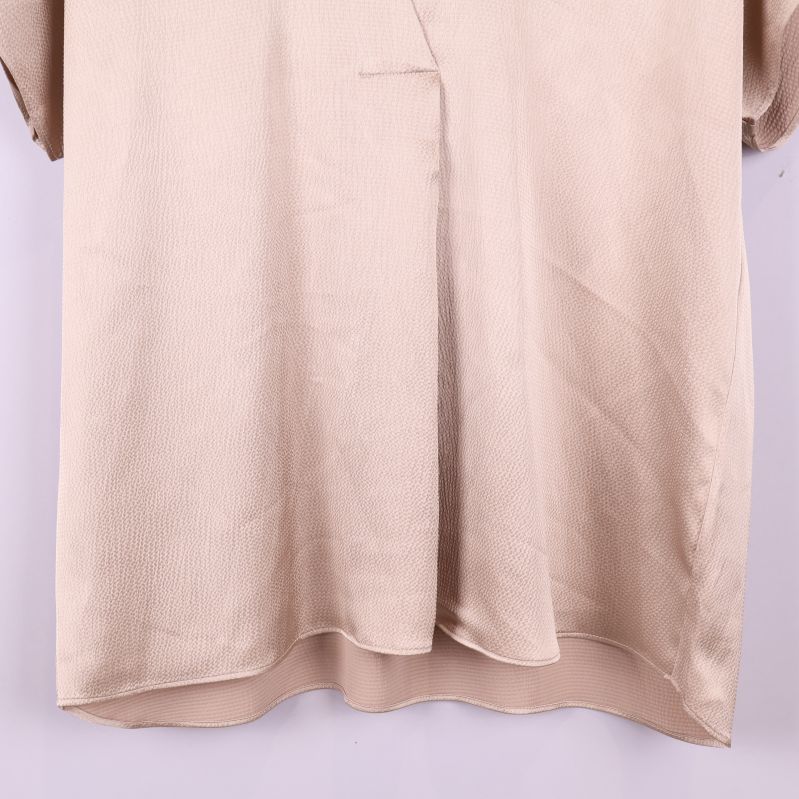 Nedre delen av blusens framsida i beige tyg