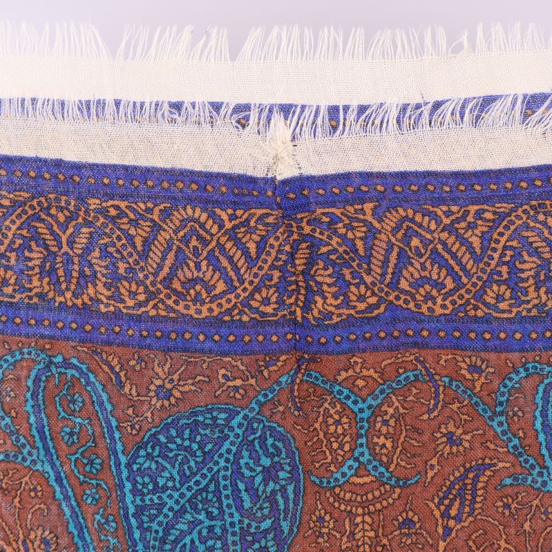Närbild på sjalens fransade kant med blå och bruna linjer