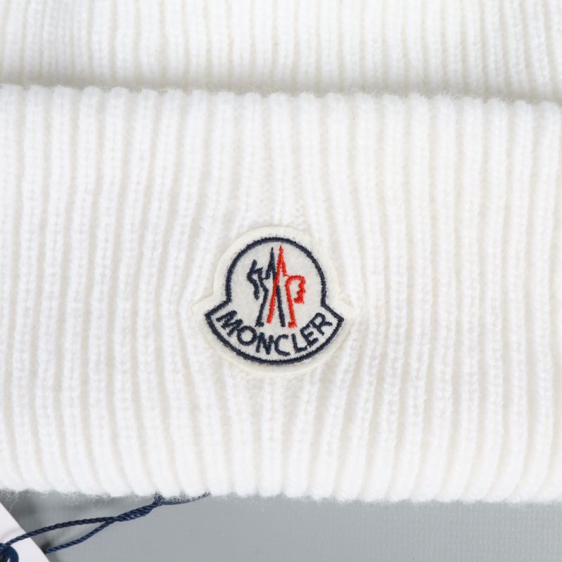 Närbild på broderad Moncler-logotyp mot vit ribbstickning