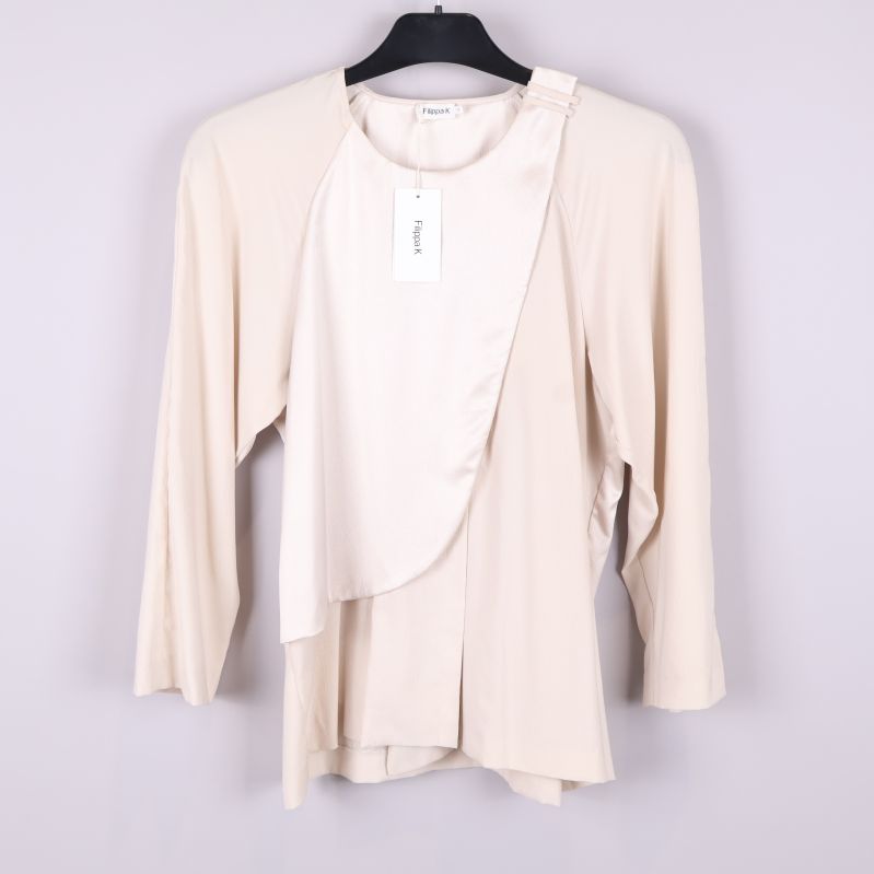 Framsida av beige omlottblus på galge mot vit bakgrund