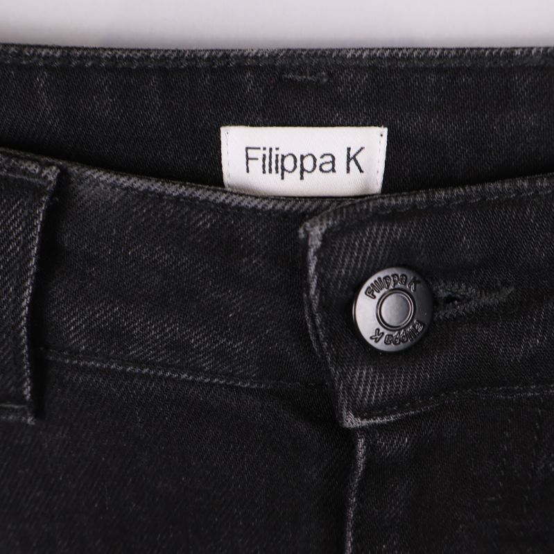 Närbild på Filippa K-logga och jeansknapp framtill