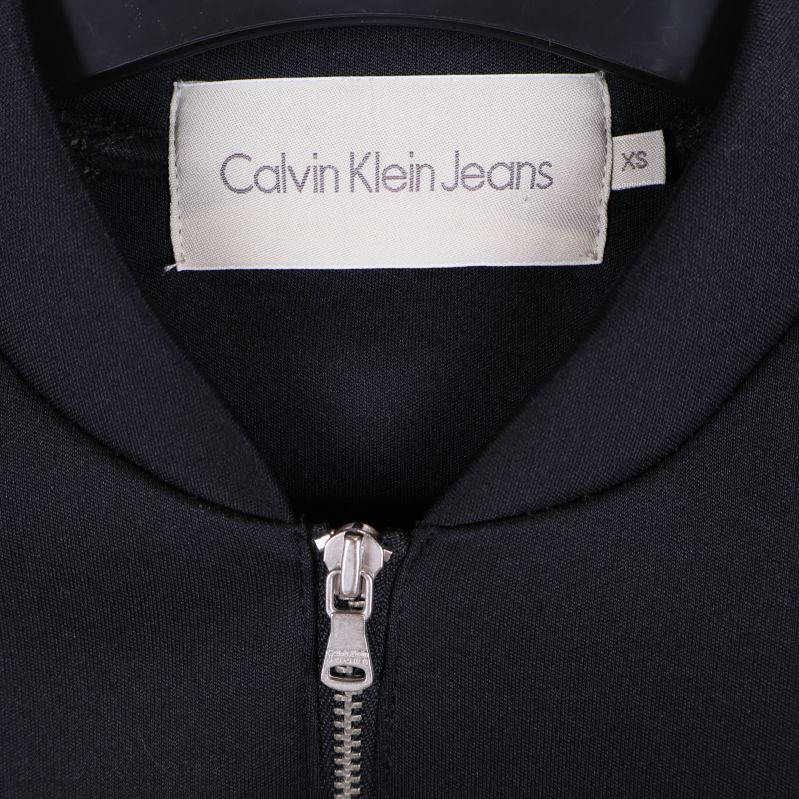 Calvin Klein Jeans etikett på insidan av svart jacka i storlek XS