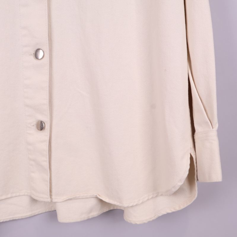 Närbild på nederkant och ärmslut av beige overshirt