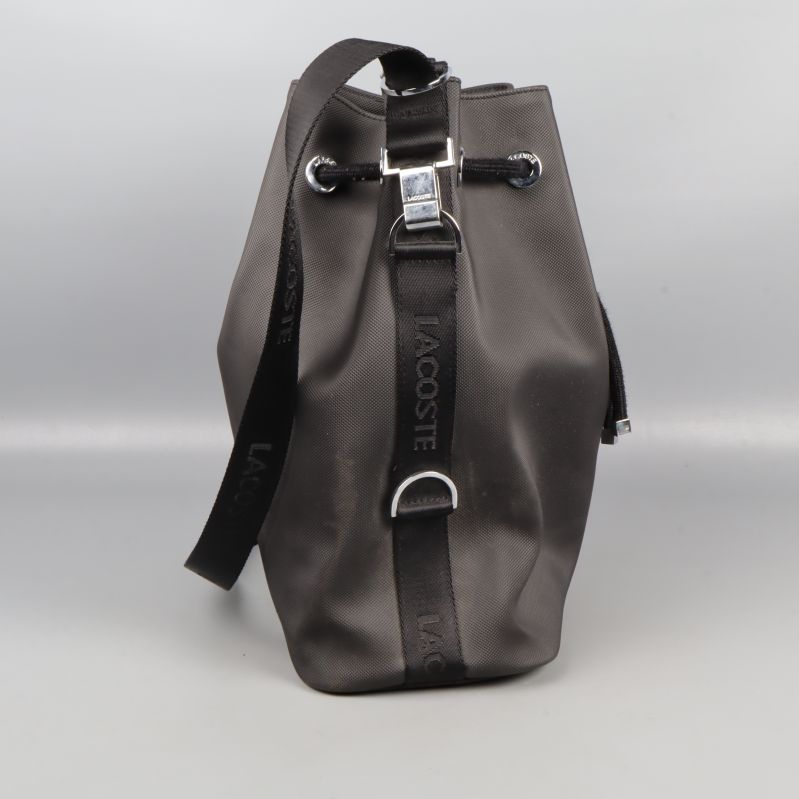 Sidovy av svart bucketbag med Lacoste-text på rem