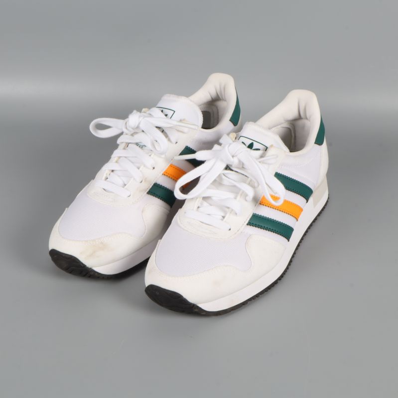 Vita sneakers med gröna och orange ränder fotograferade snett framifrån