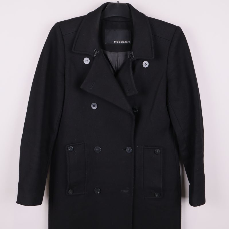 Övre delen av svart rock med synliga knappar och krage