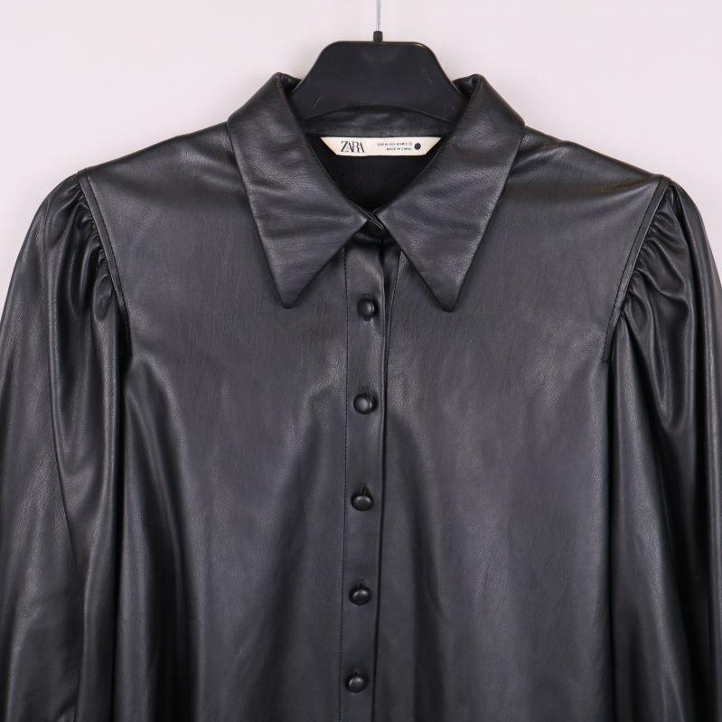 Närbild på krage och knäppning på svart blus i konstläder