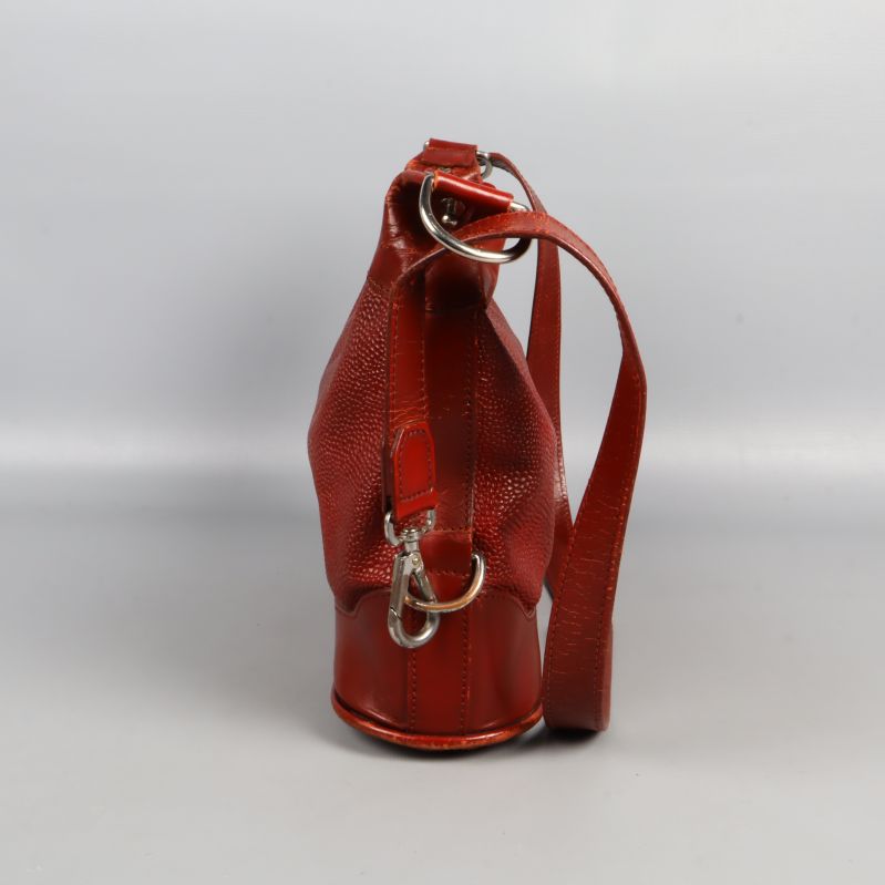 Röd axelremsväska sedd från vänster sida med metalldetaljer