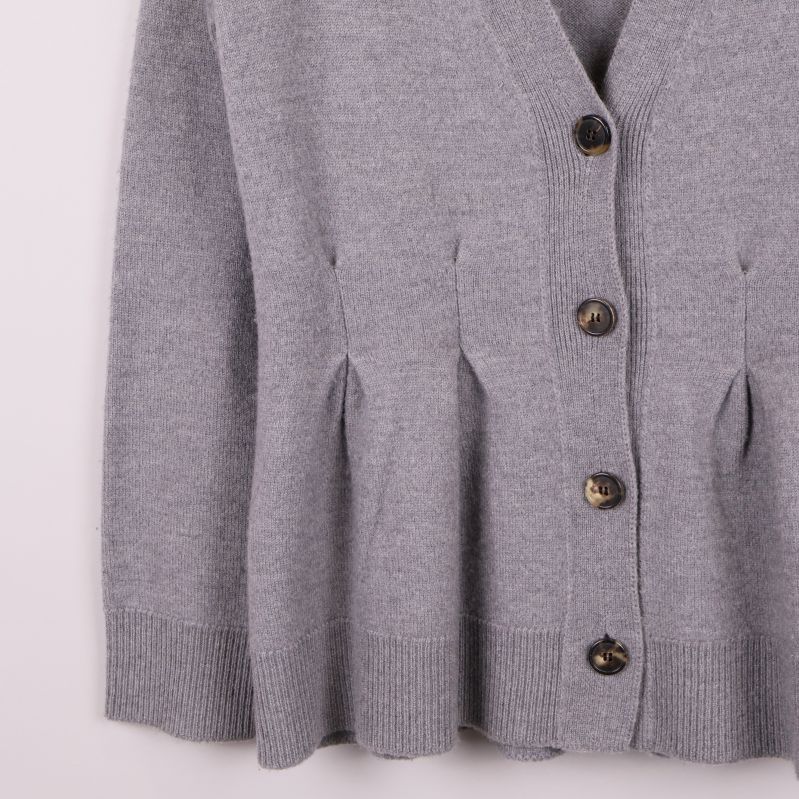Nederdelen av grå kofta med knappar och veckade detaljer