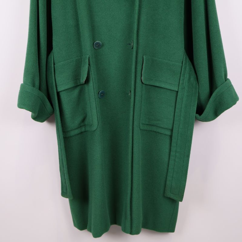 Detaljbild på fickor och nederkant av grön kappa