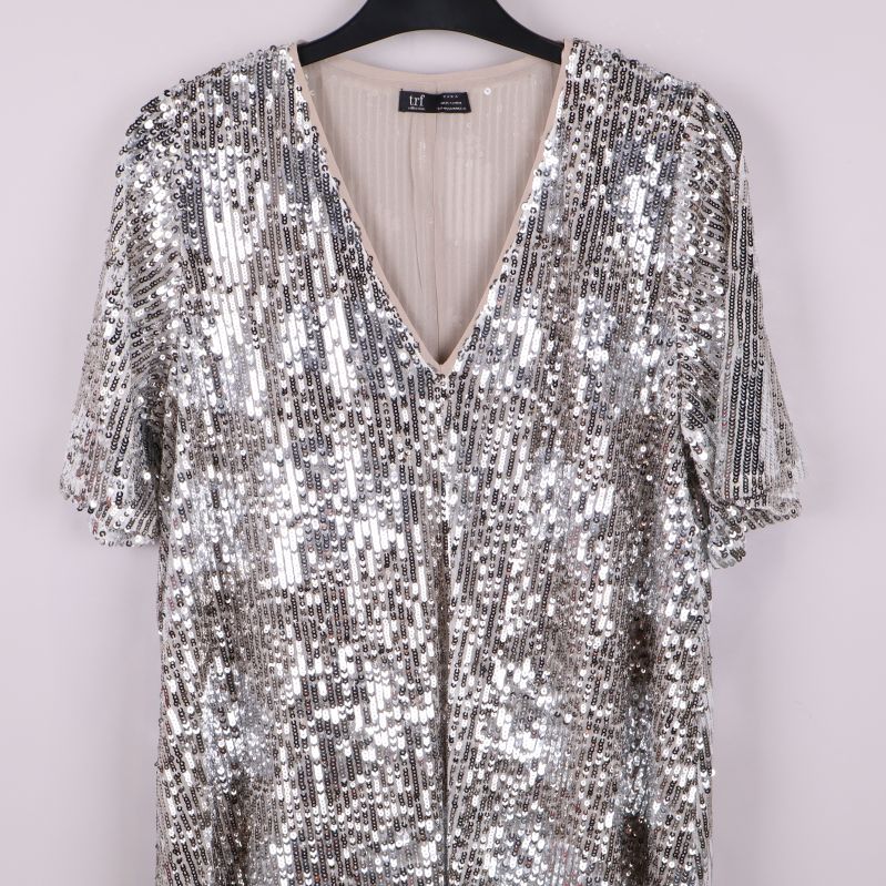 Närbild på v-ringning och paljetter framtill på tunikan