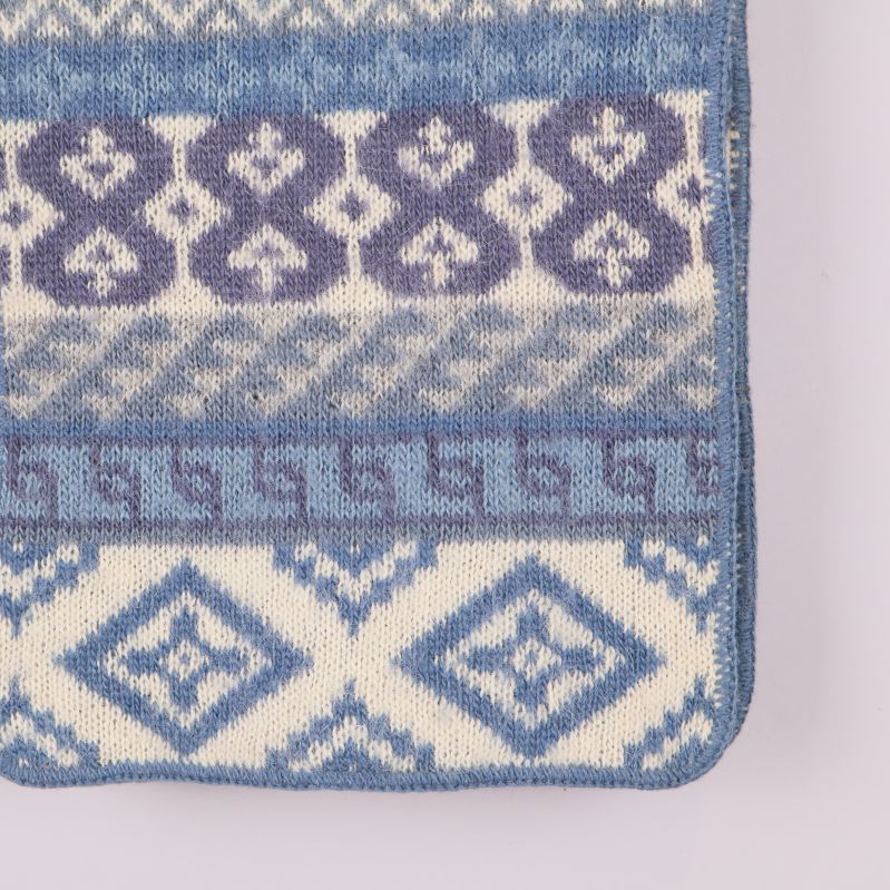 Närbild på hörn av stickad halsduk med blått och vitt mönster