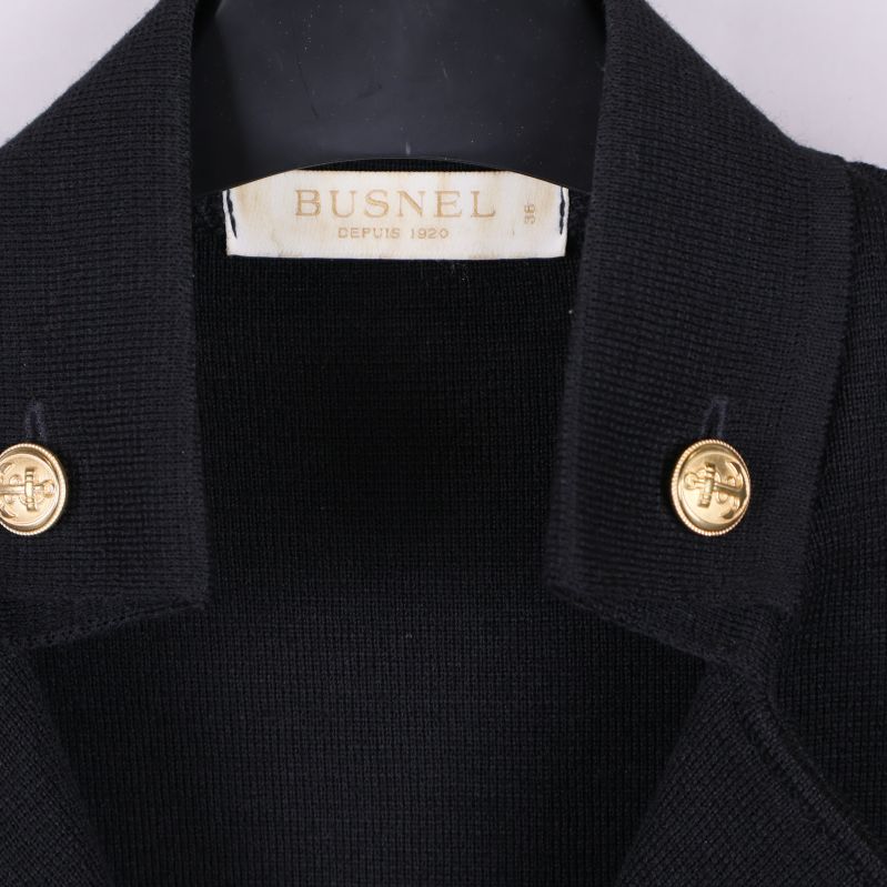 Närbild på Busnel-logotyp och krage med guldknappar