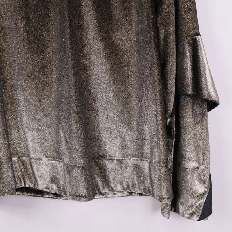 Närbild på nederkant av topp och ärm i glittrigt tyg