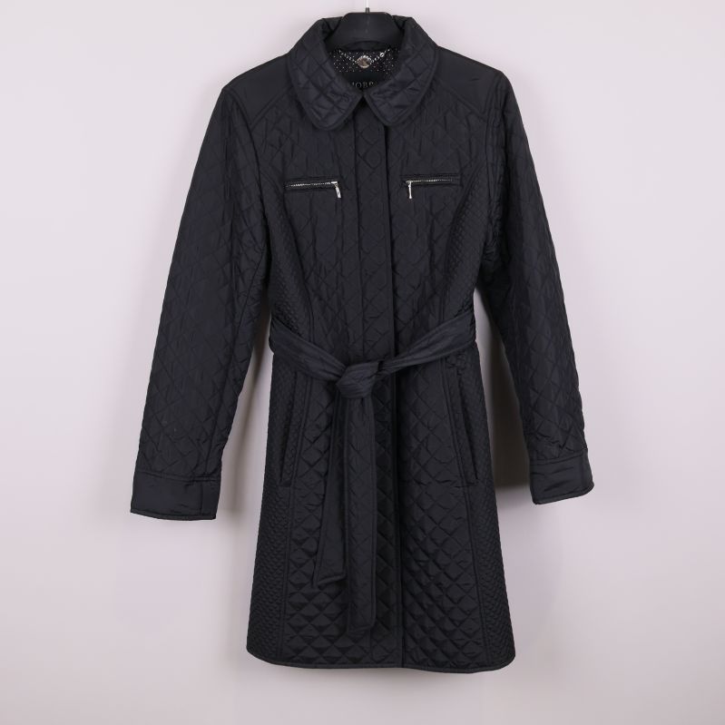 Svart quiltad jacka med skärp framifrån mot vit bakgrund