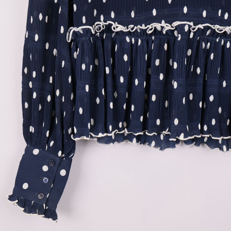Närbild på ärmslut och knappar med volangkant i blått prickigt tyg