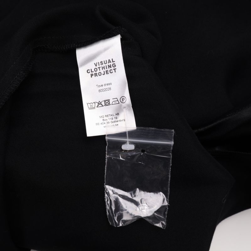 Tvättrådsetikett med varumärkesnamn och liten plastpåse med extra knapp