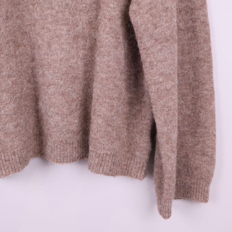 Närbild på nederkant och ärmslut av beige tröja