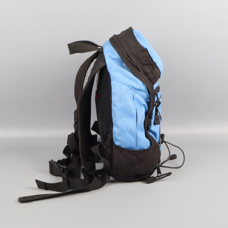 Blåsvart ryggsäck från sidan med dragkedjefickor och snörning