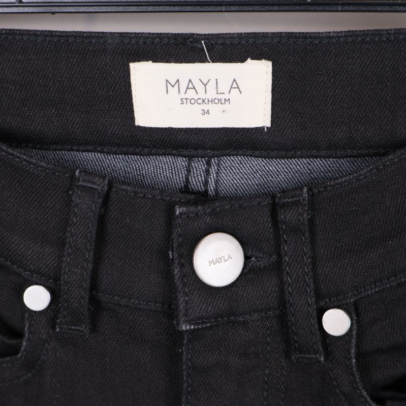 Närbild av Mayla Stockholm etikett och knapp i midjan på svarta jeans