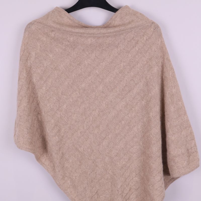 Närbild på beige poncho med diskret stickat mönster