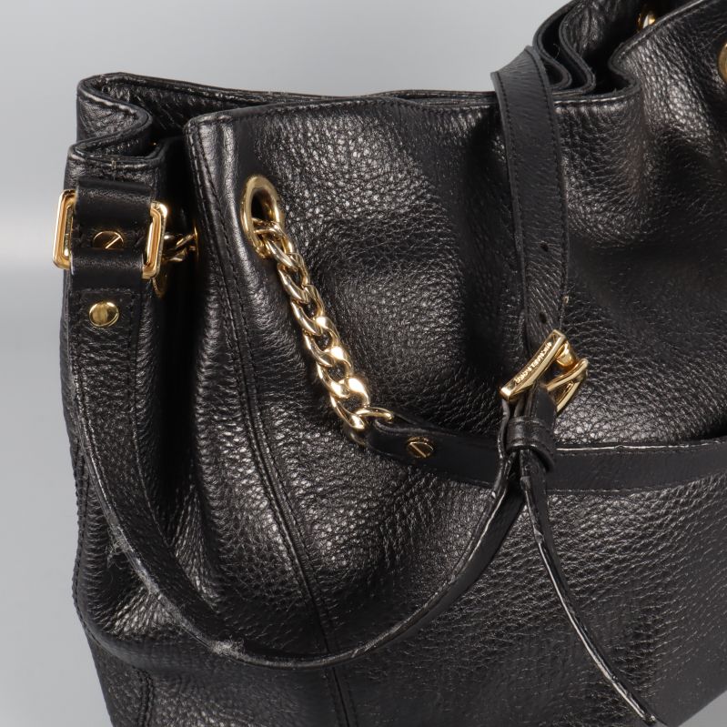 Närbild på guldkedja och spänne på svart väska