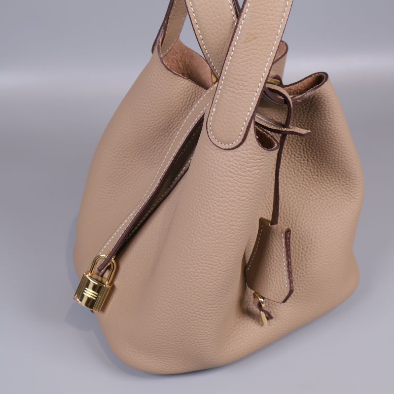 Närbild på beige bucketväska med lås och metallhänge